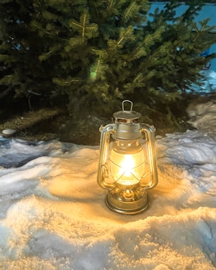 Cozy winter scene with a glowing lantern beside a snow-covered pine tree.