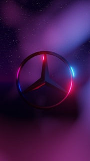 A metallic logo with a circular shape and three-pointed star inside is highlighted against a backdrop featuring gradients of deep blue, purple, and pink. The star and circle are illuminated with neon hues, creating a futuristic and sleek appearance. A starry sky adds depth to the background.