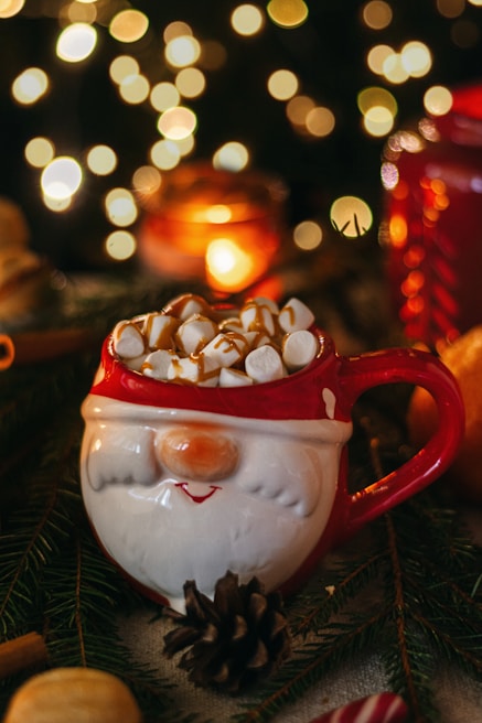 A close-up of a ceramic mug featuring a cheerful Santa Claus design, filled with hot cocoa and marshmallows.