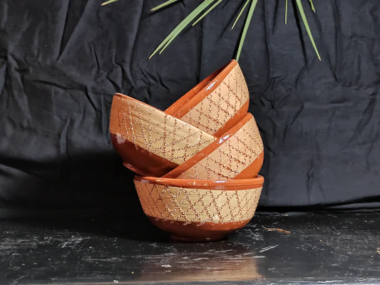 A close-up of textured, durable stoneware bowls stacked beside a blooming houseplant.