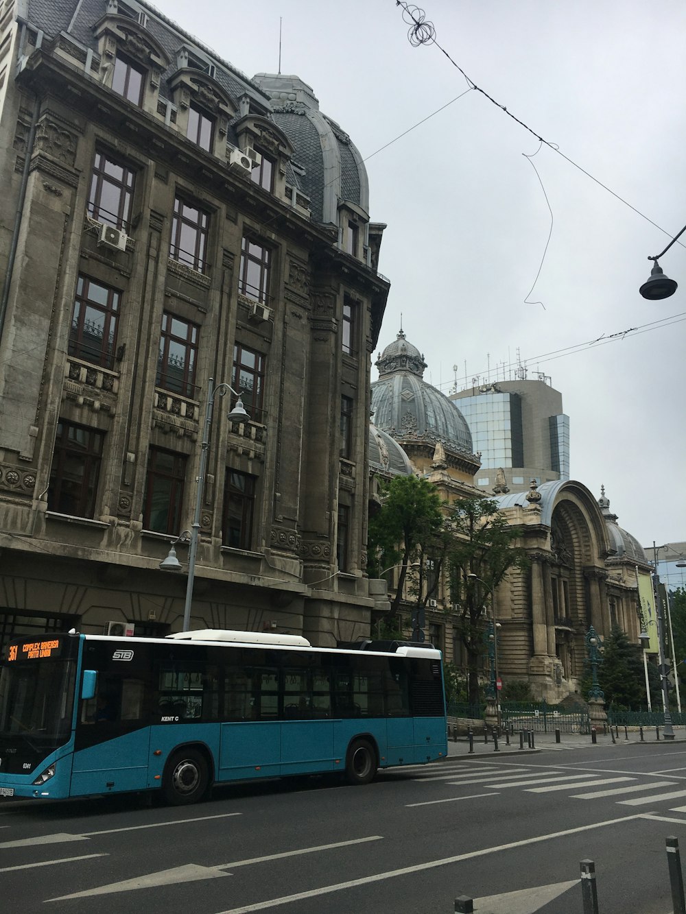 a blue bus driving down a street next to a tall building