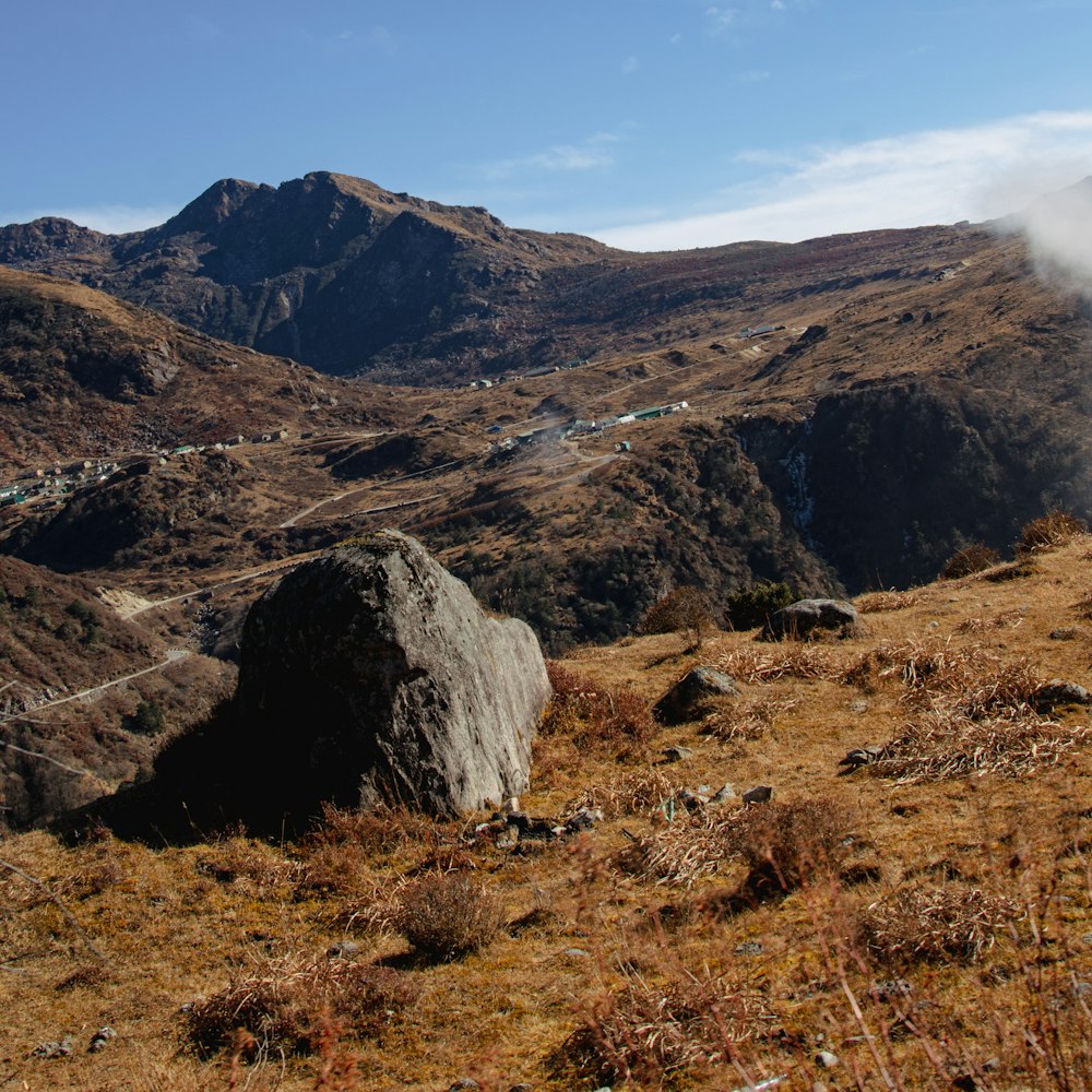 a large rock sitting on top of a grass covered hillside