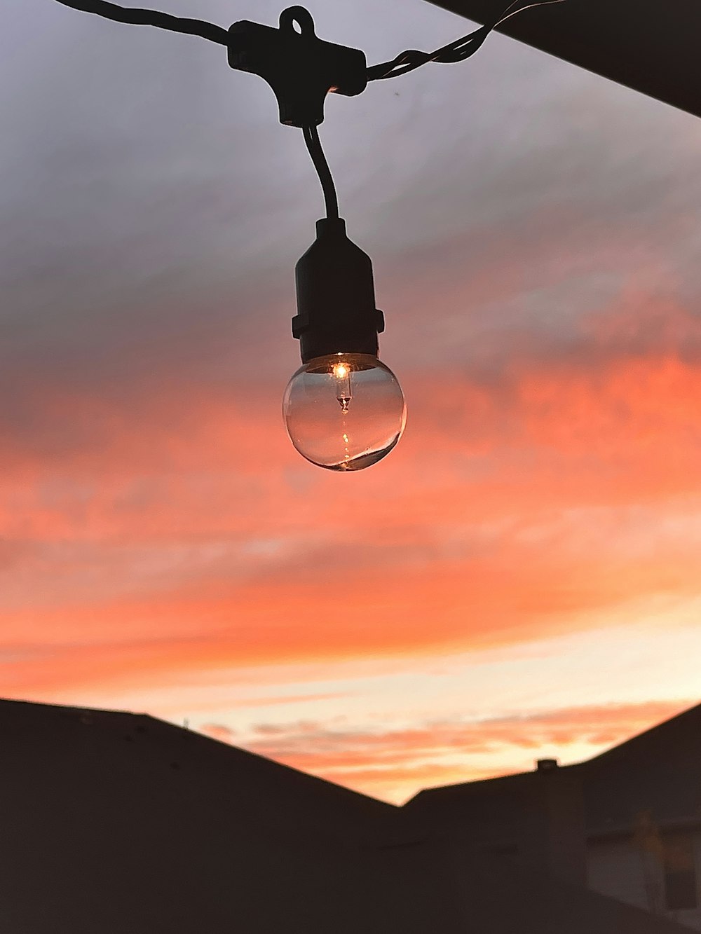 a light bulb hanging from a wire with a sunset in the background