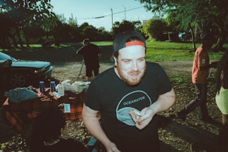 A laid-back American backyard barbecue scene with friends wearing Poor Bastard Company shirts and hats.