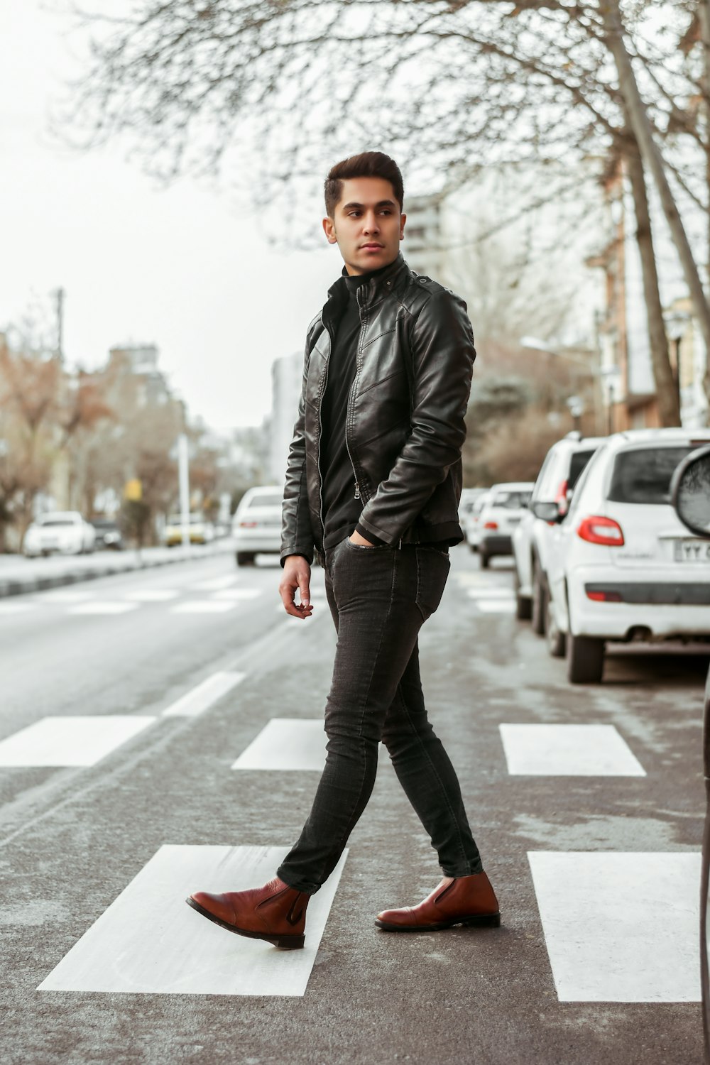 a man in a leather jacket crossing a street