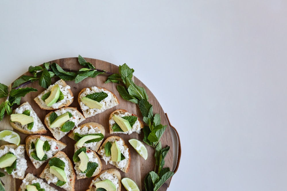 a wooden plate topped with slices of bread covered in cheese and avocado