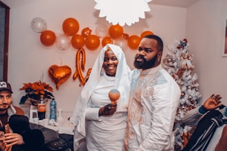 A happy couple smiling together, surrounded by their supportive families in a cozy home setting.