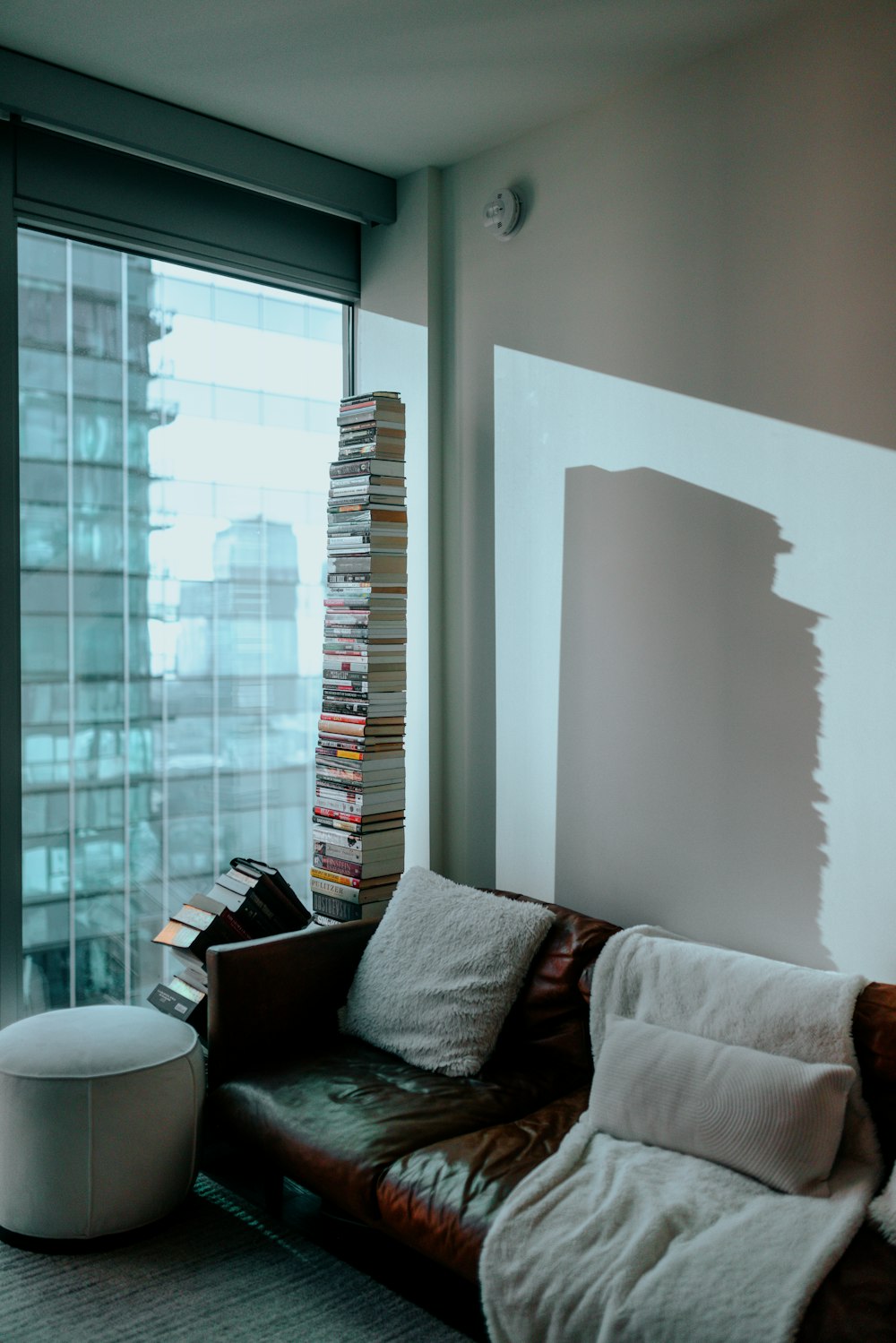 a living room with a brown leather couch and a tall stack of books