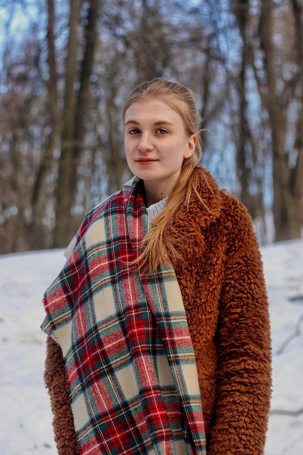 a woman standing in the snow wearing a plaid blanket