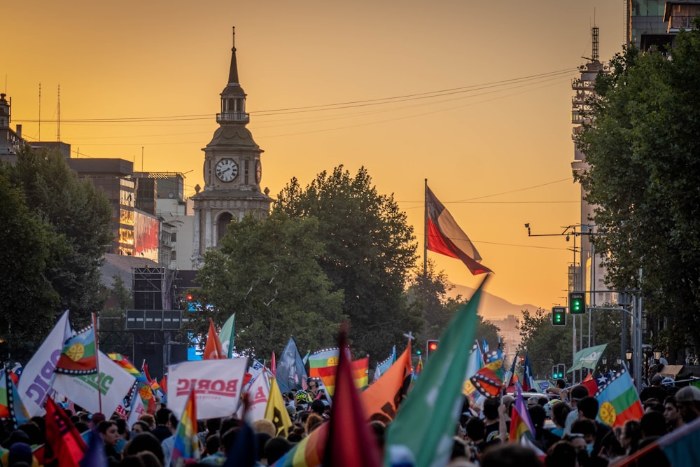 a crowd of people holding flags and a clock tower in the background