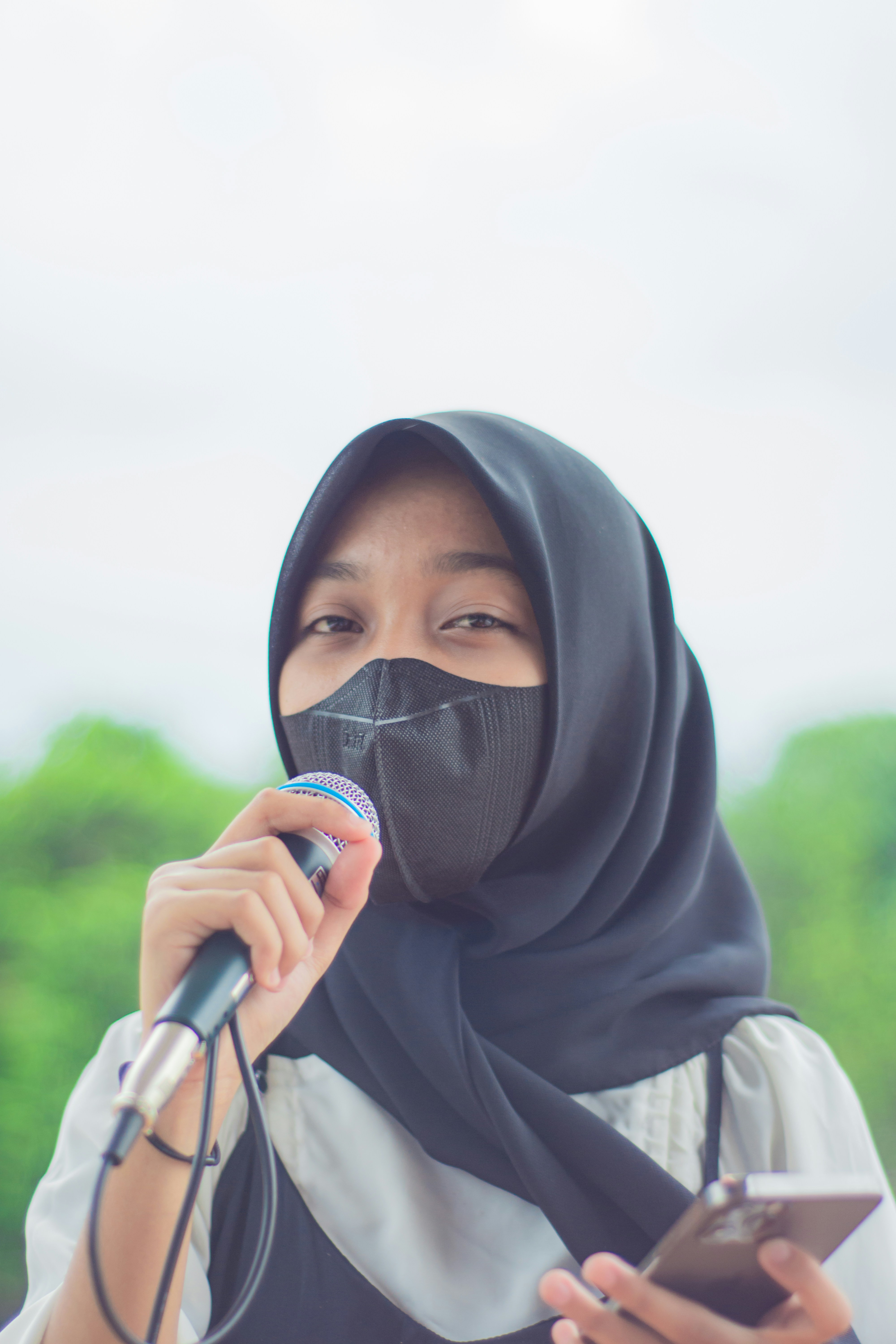 a woman in a hijab holding a microphone and a cell phone