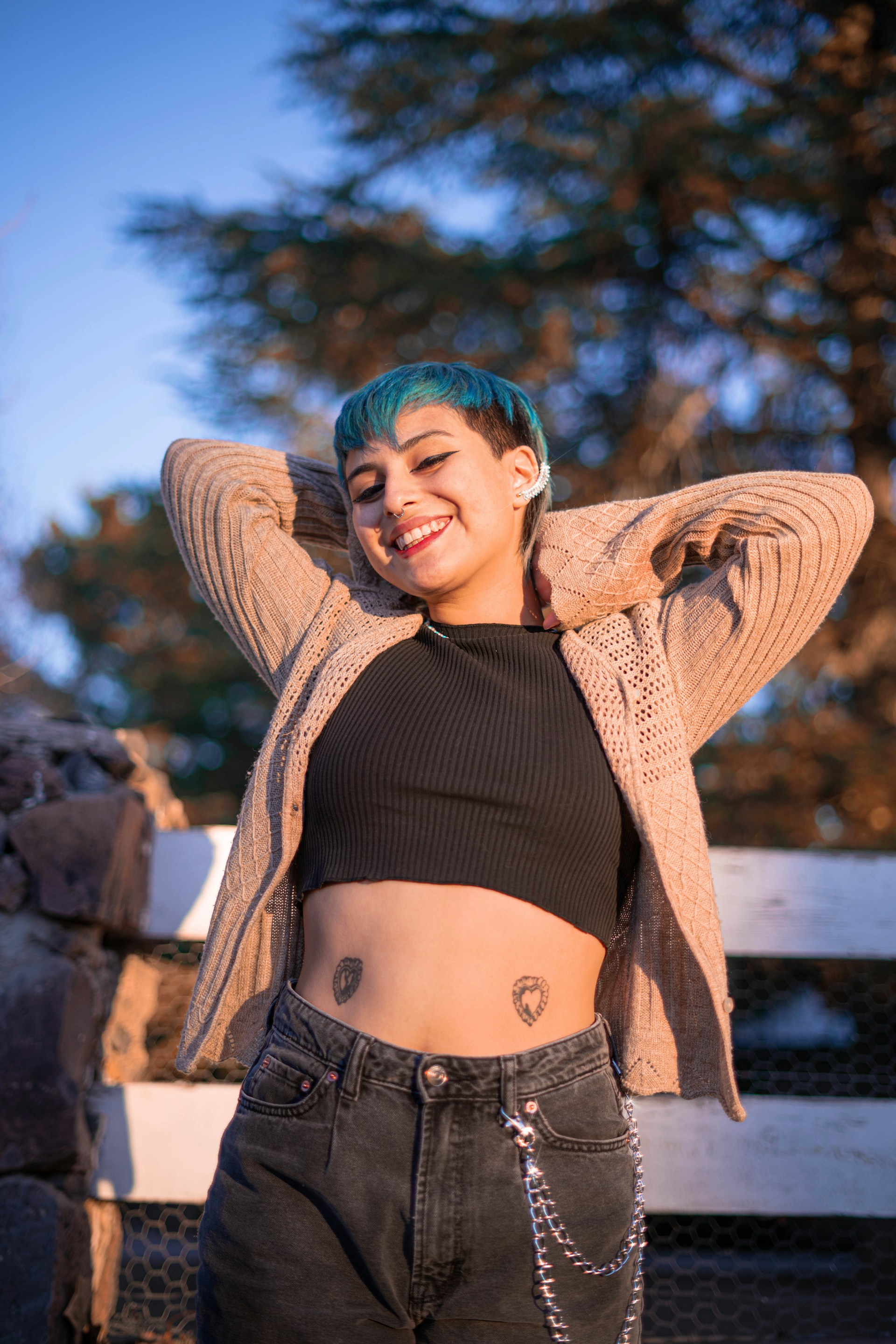 a woman with blue hair and piercings standing in front of a fence
