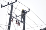 A person wearing a safety harness and helmet is working high on an electrical pole surrounded by wires.