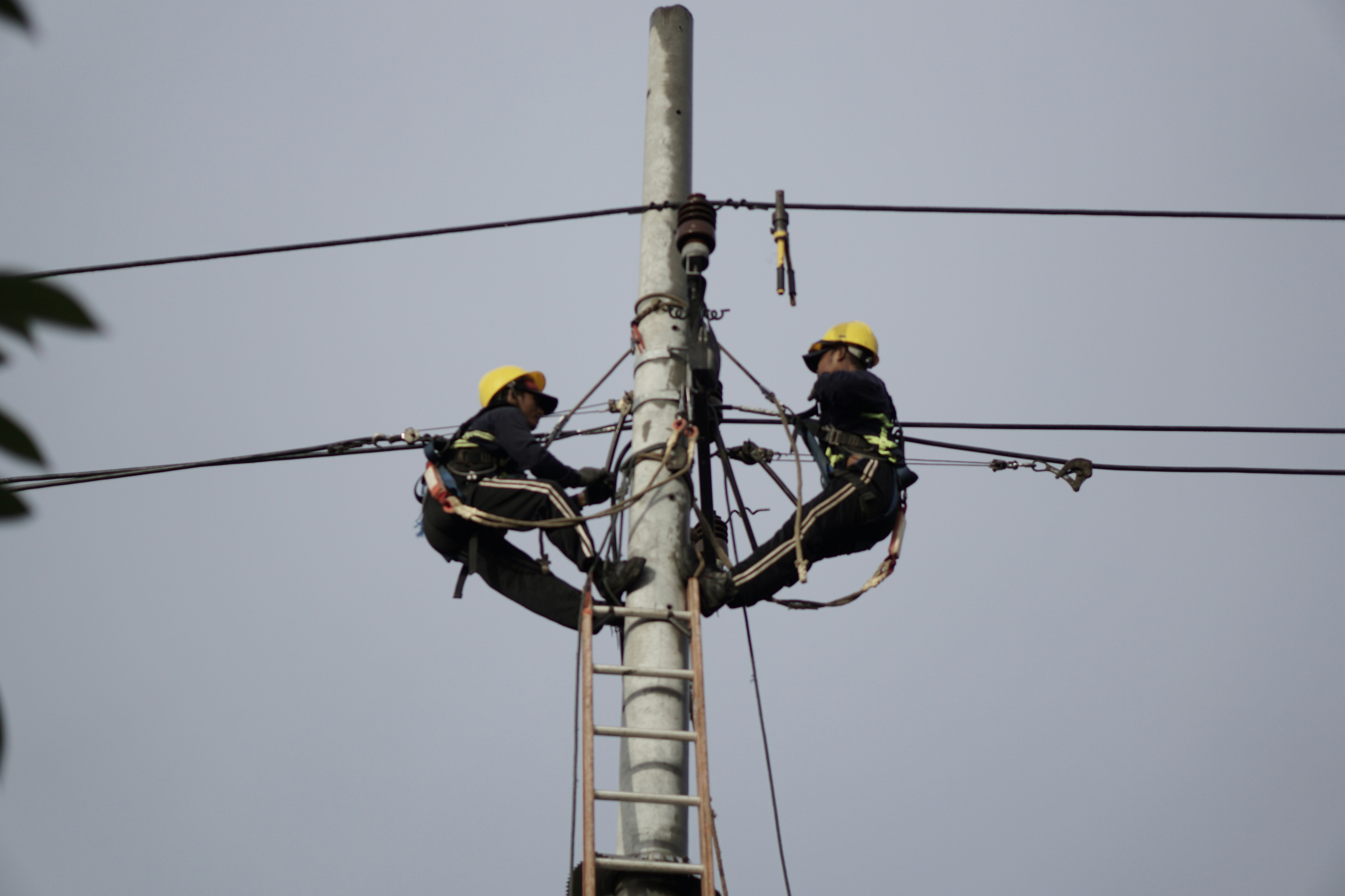 a couple of men standing on top of a power pole