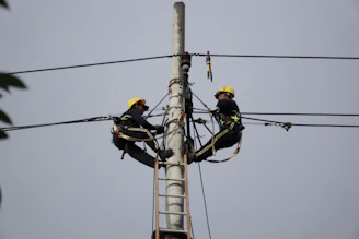 a couple of men standing on top of a power pole