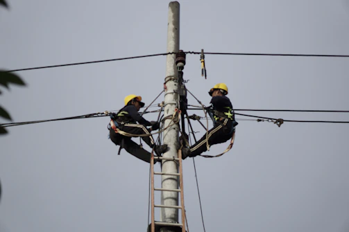 a couple of men standing on top of a power pole
