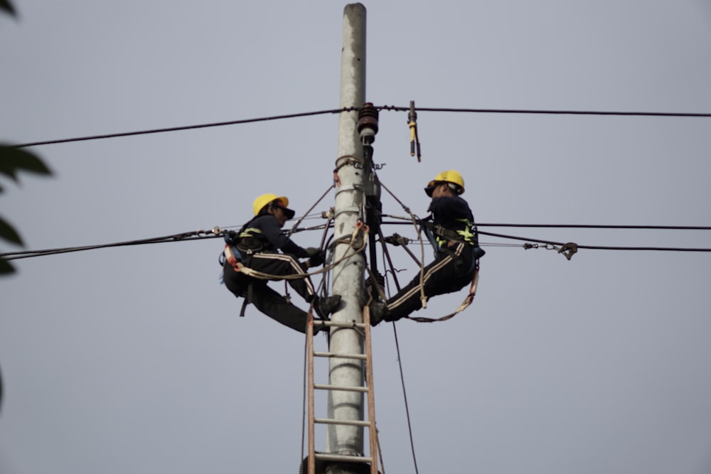 a couple of men standing on top of a power pole