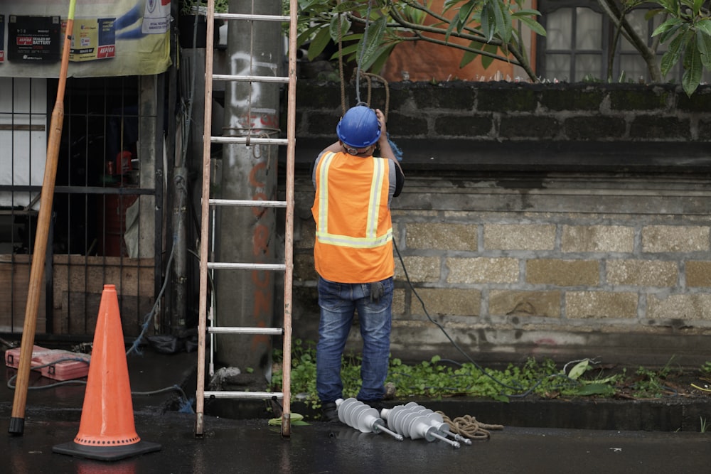 a man in an orange vest and safety vest standing next to a ladder