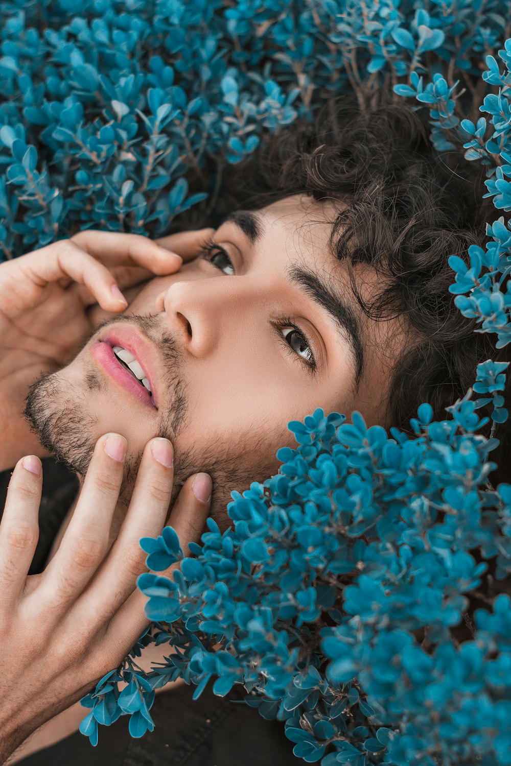 a man with curly hair and blue flowers around his neck