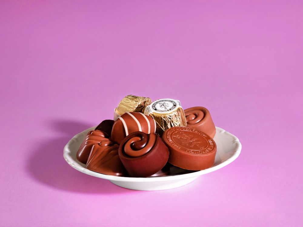 a white bowl filled with assorted chocolates on a pink background