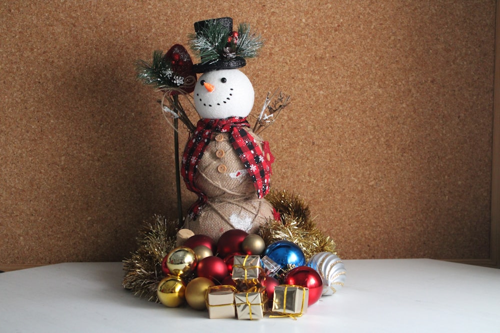 a snowman sitting on top of a table surrounded by christmas ornaments