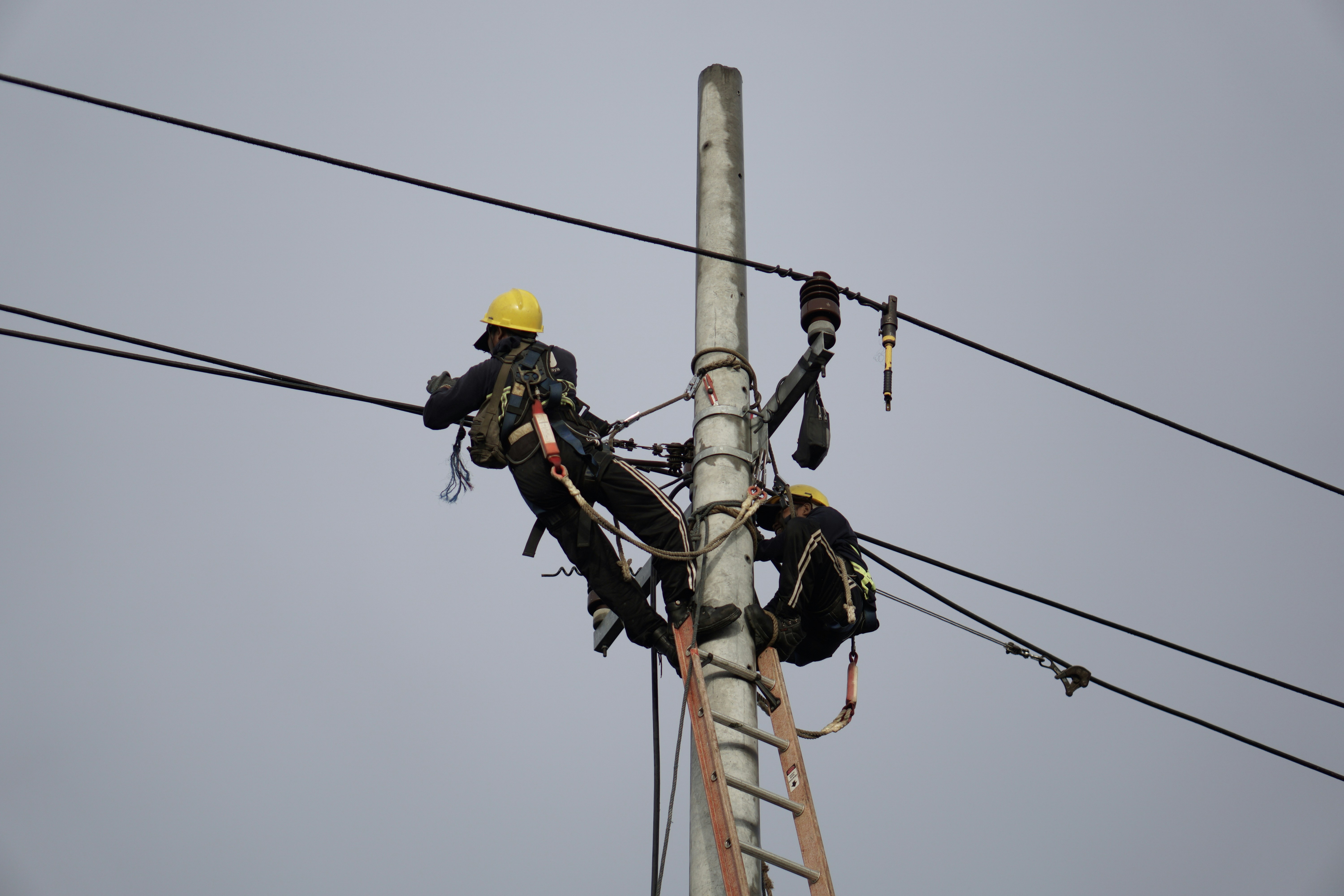 a couple of men standing on top of a power pole