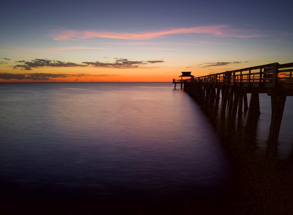a long pier stretches out into the ocean at sunset