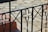 An ornate black metal railing with floral and geometric patterns in the foreground, set against a background of a light stone patio.