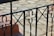 An ornate black metal railing with floral and geometric patterns in the foreground, set against a background of a light stone patio.