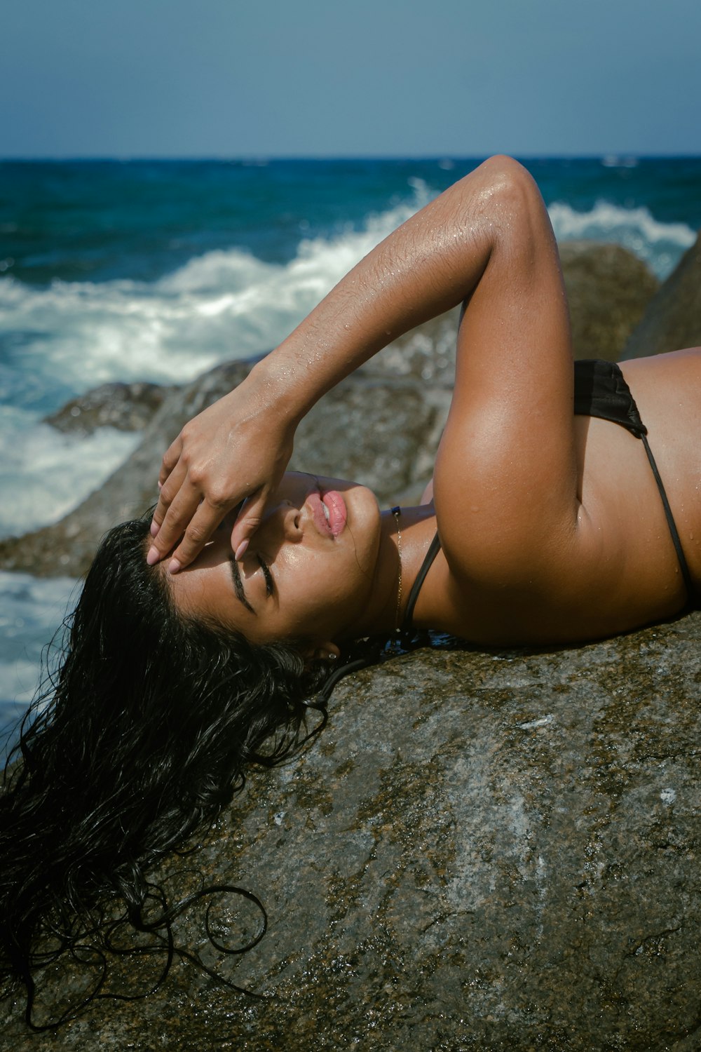 a woman laying on top of a rock next to the ocean