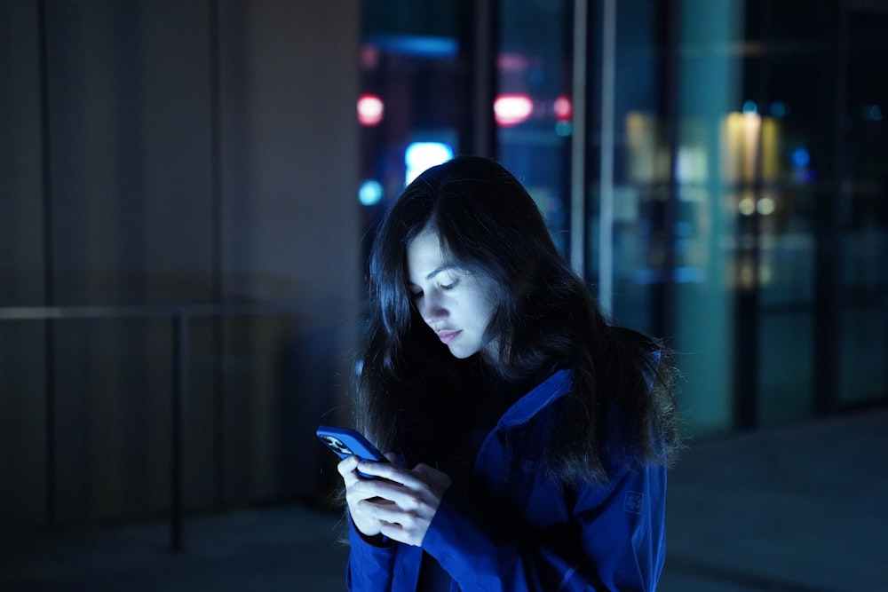 携帯電話を見ている青いジャケットを着た女性