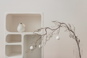 a vase with a branch in it next to a shelf with ornaments