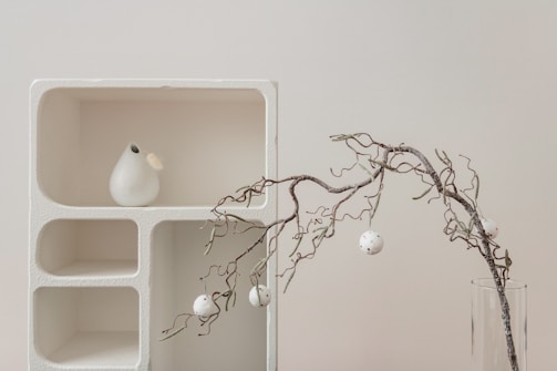 Close-up of a stylish golden vase and delicate ornaments arranged on a minimalist shelf