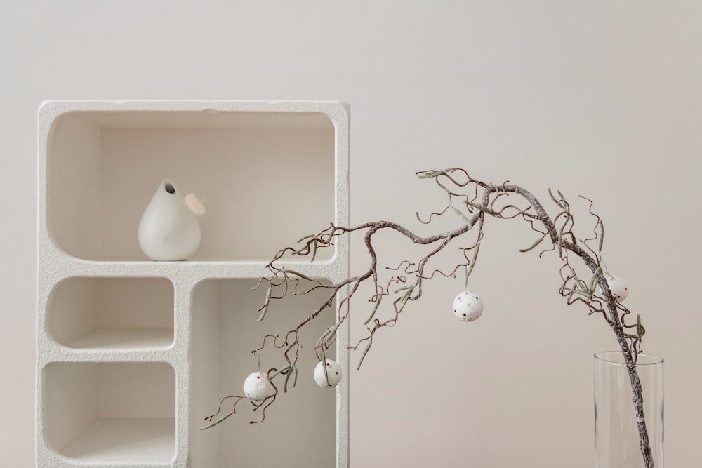 a vase with a branch in it next to a shelf with ornaments