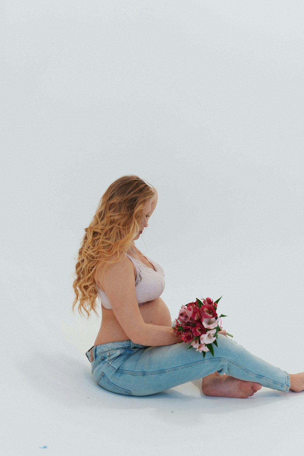 a pregnant woman sitting on the floor with a bouquet of flowers