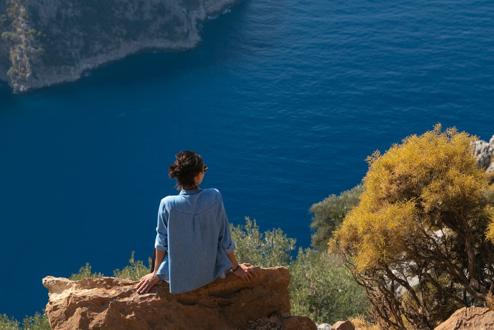 a person sitting on a rock looking at the water