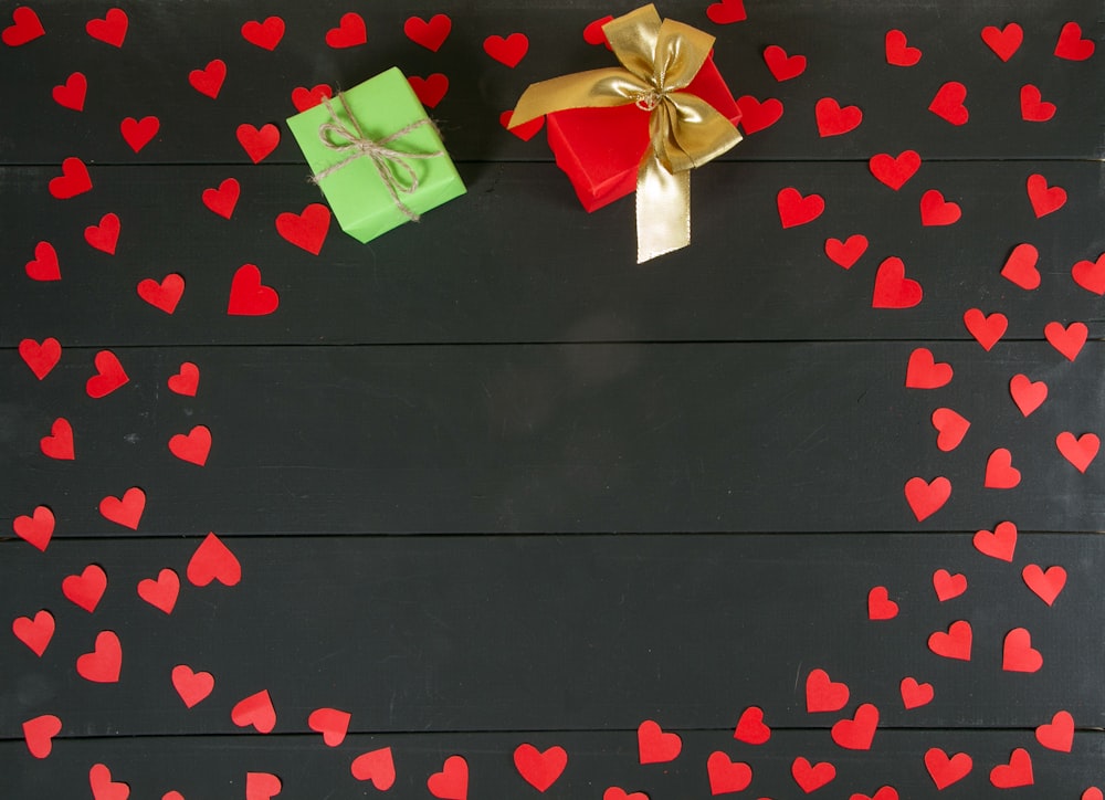 um fundo preto com corações vermelhos e uma caixa de presente verde