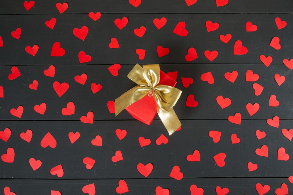 a red and gold bow with hearts on a black background