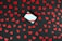 A black wooden surface is scattered with numerous red heart-shaped cutouts. In the center sits a small white gift box adorned with diagonal red stripes.