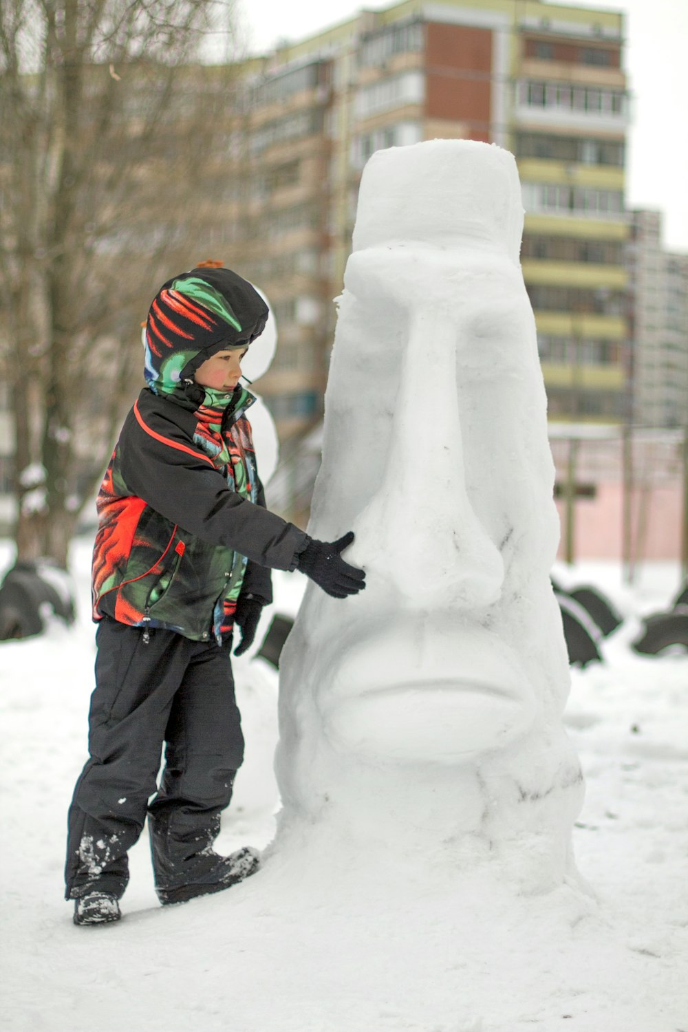 um menino de pé ao lado de uma escultura de neve