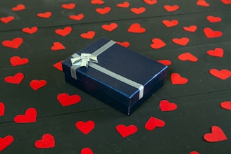a blue gift box with a bow on a black surface with red hearts