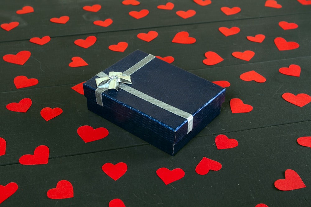 Un coffret cadeau bleu avec un nœud sur une surface noire avec des cœurs rouges