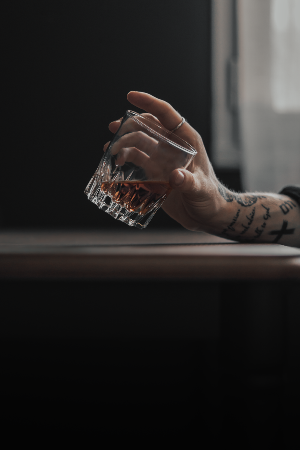 a person with tattoos holding a glass of alcohol