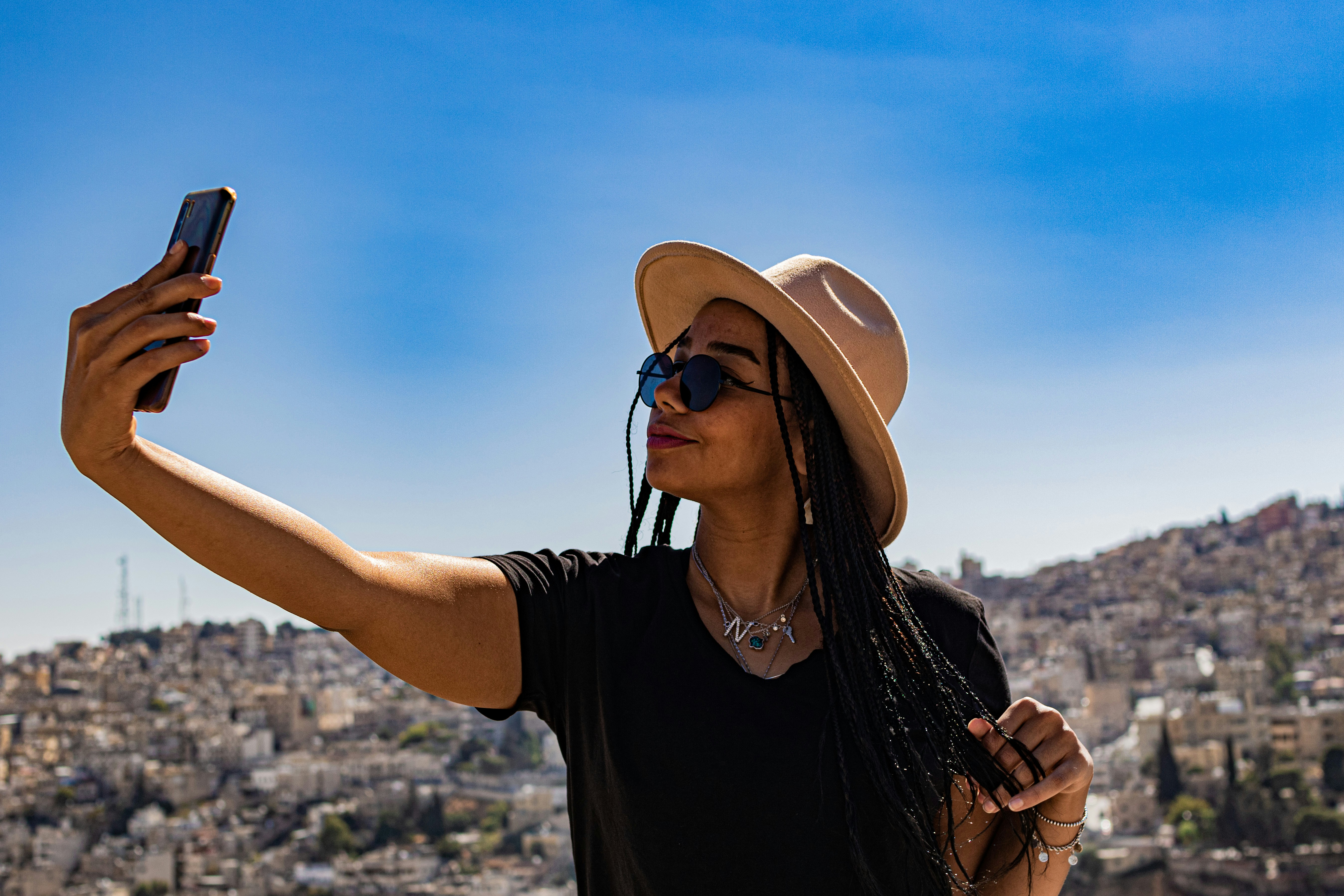 a woman wearing a hat and sunglasses taking a selfie, Woman in a hat taking a selfie