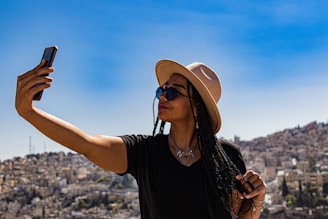 a woman wearing a hat and sunglasses taking a selfie