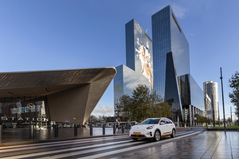 a white car driving down a street next to tall buildings