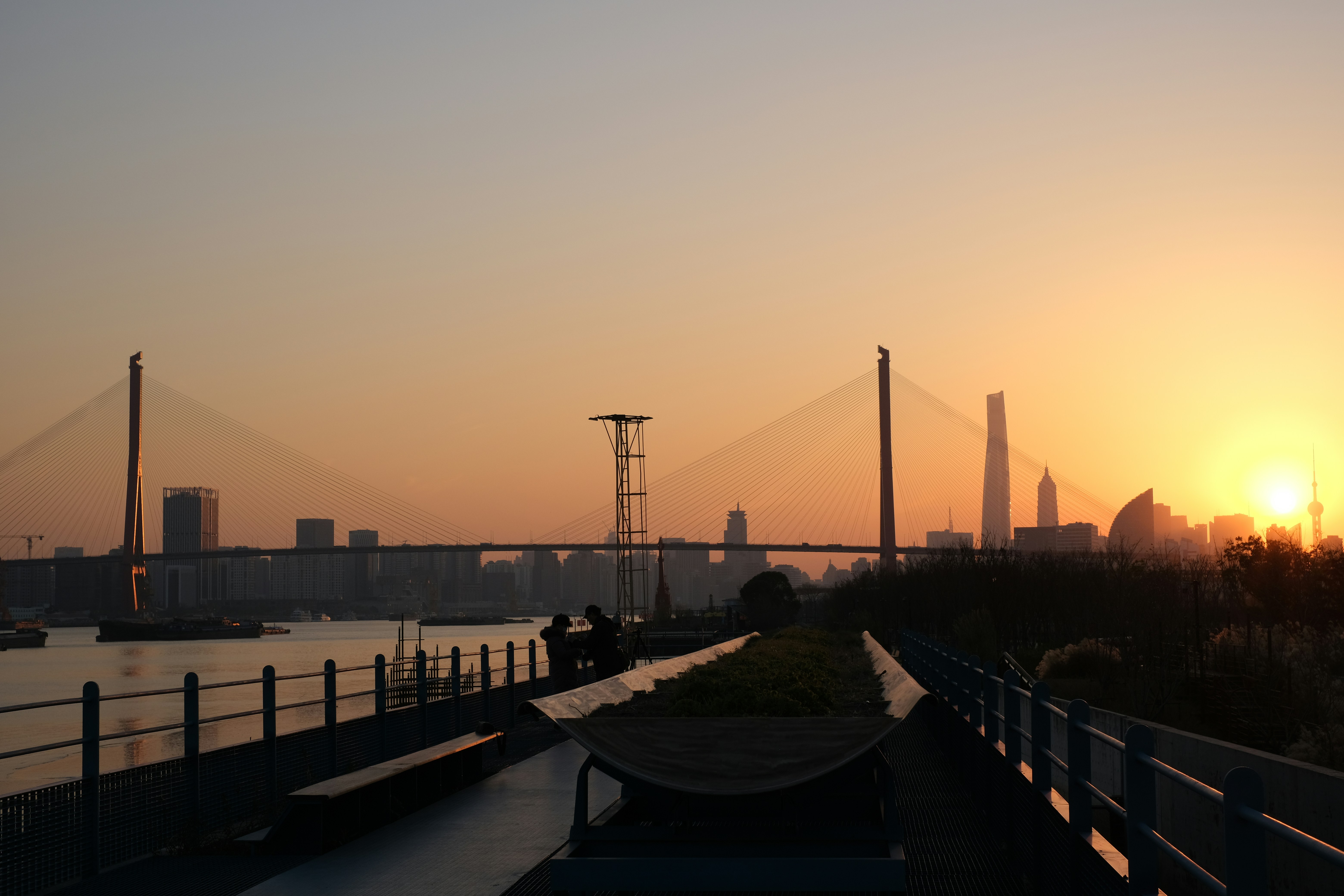 the sun is setting behind a bridge and a body of water