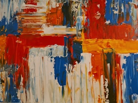 Bold, abstract art featuring vibrant blocks and strokes of color, including red, blue, orange, and white. The painting consists of thick, textured brushstrokes and dynamic patterns that evoke movement and energy.