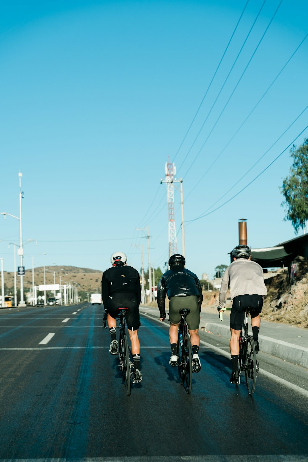 three bicyclists riding down the road on a sunny day