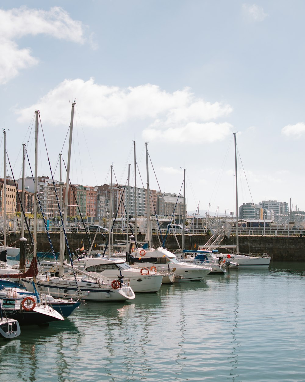 a harbor filled with lots of sailboats under a cloudy blue sky